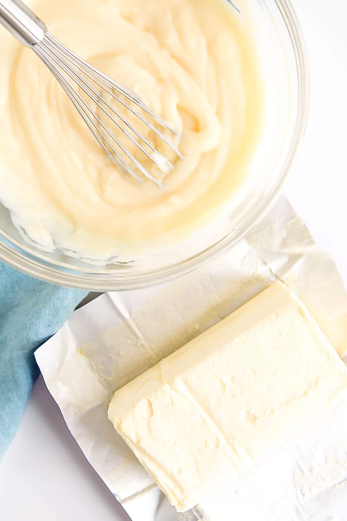 Pastry cream in a bowl with a whisk and butter next to it.