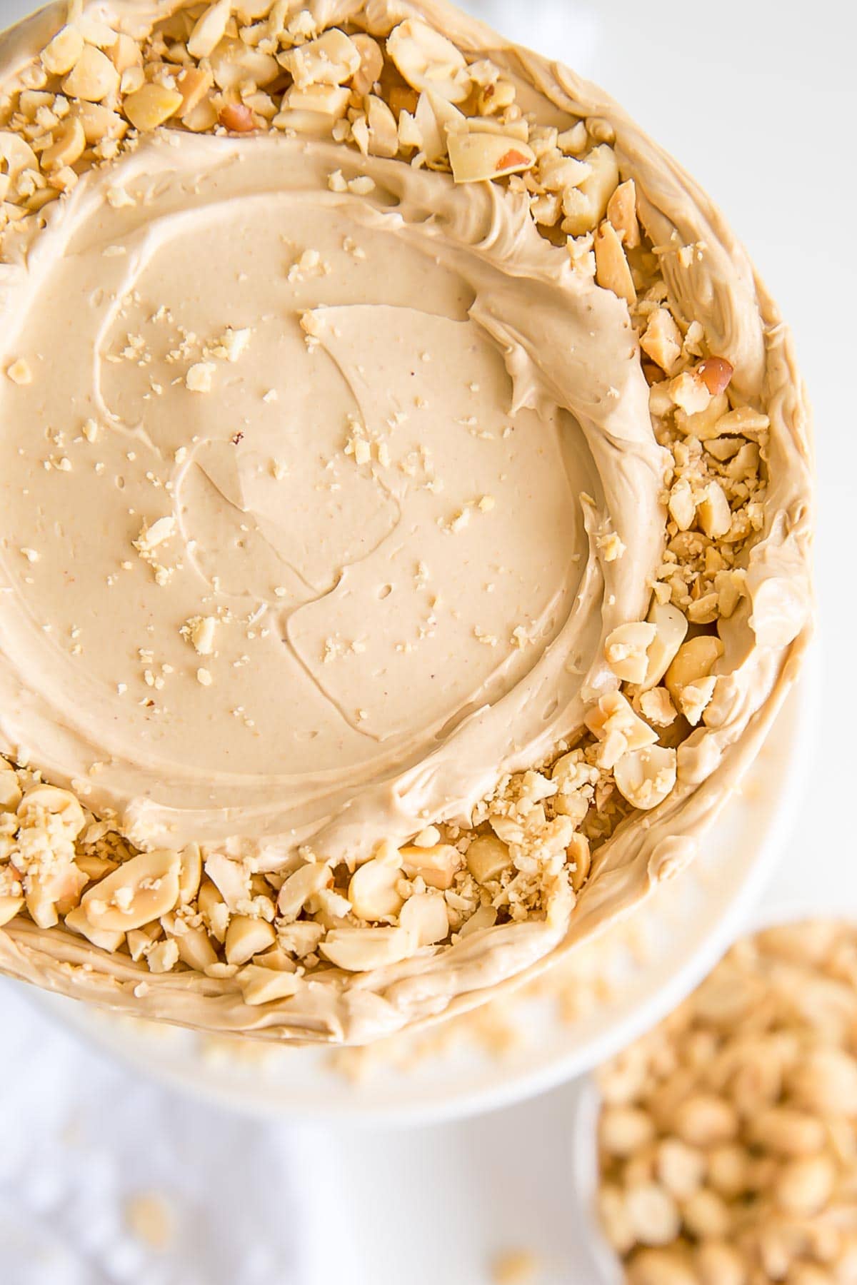 Peanut butter lovers, this cake is for you! Peanut butter cake layers studded with peanut butter chips covered in a peanut butter Swiss meringue buttercream. | livforcake.com Top view of the cake showing fresh chopped peanuts and a rustic frosting.